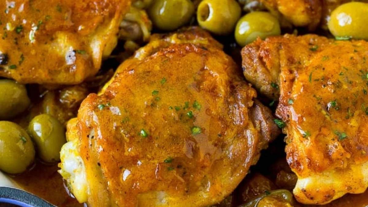 A plate with chicken and olives in a sauce.