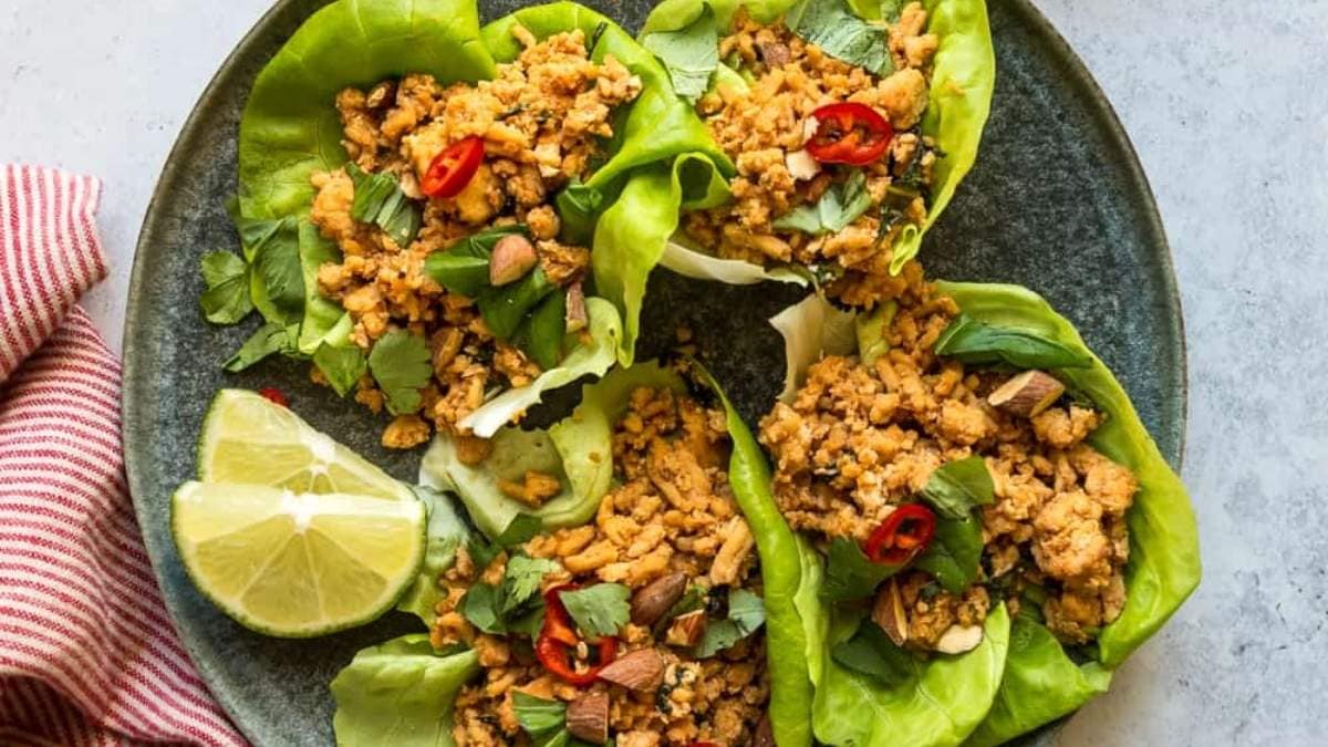 Thai chicken lettuce wraps on a plate with lime wedges.