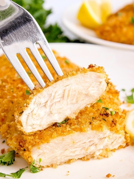 A piece of chicken on a plate with a fork.