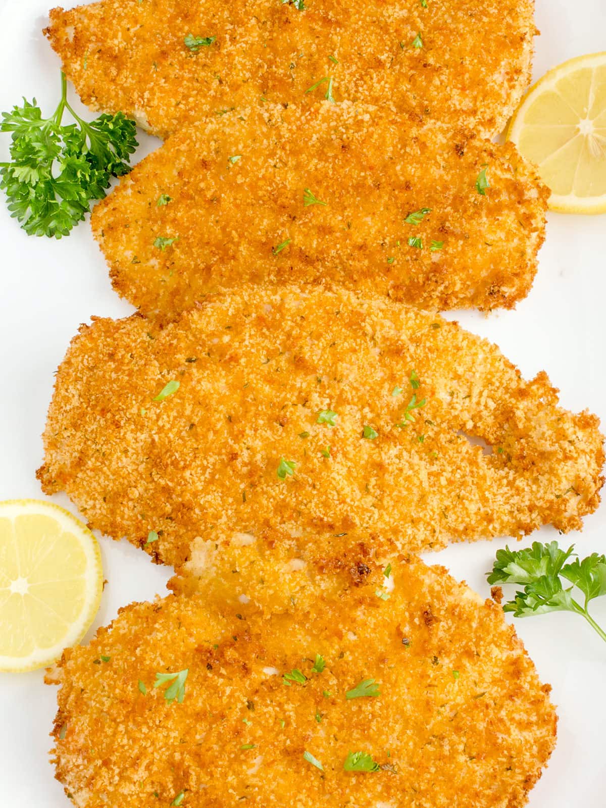 Air-fried fish fillets on a white plate with lemon wedges.