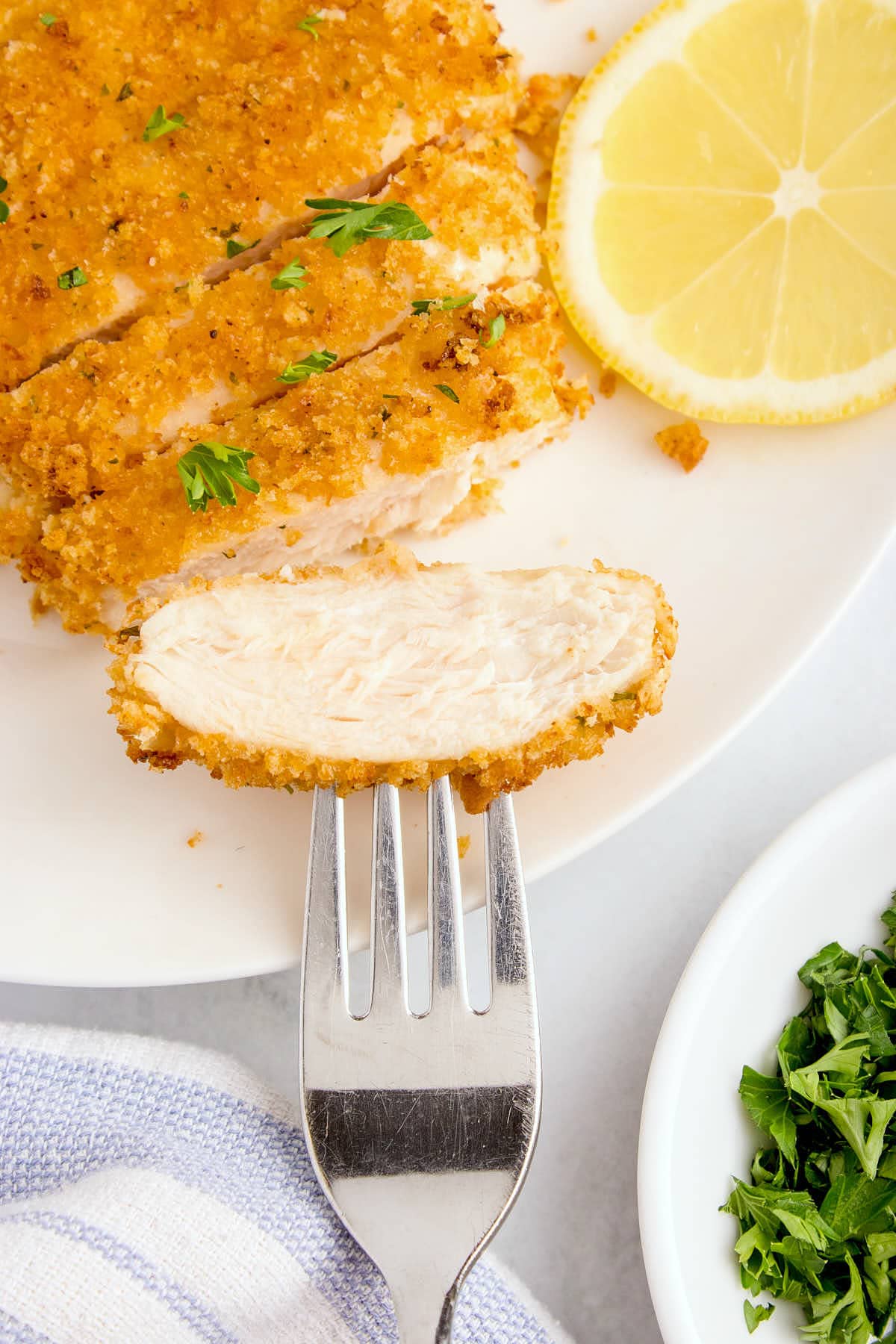 Air fryer chicken cutlets with lemon and parsley on a plate with a fork.