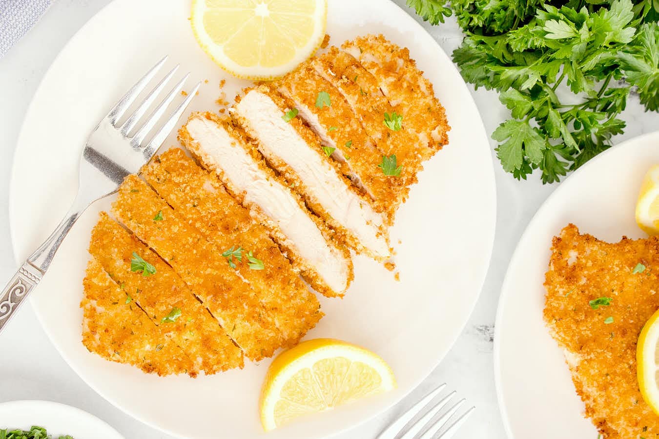 A plate with chicken cutlets and lemon wedges on it.