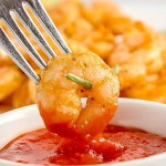 A fork is dipping Thai Red Curry Chicken into a bowl of sauce.