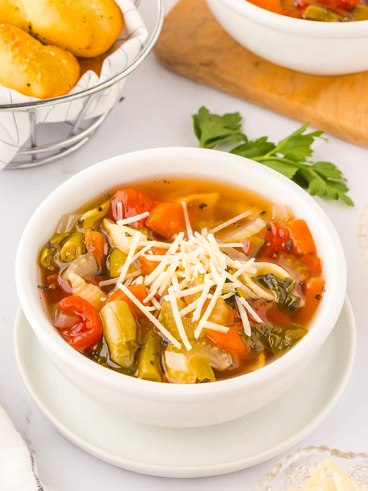 A bowl of vegetable soup with bread on a table.