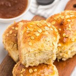 A wooden cutting board with Oatmeal Rolls and sauce on it.