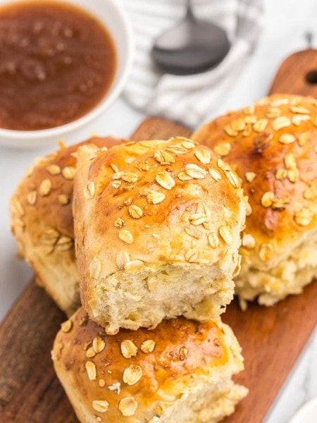 A wooden cutting board with Oatmeal Rolls and sauce on it.