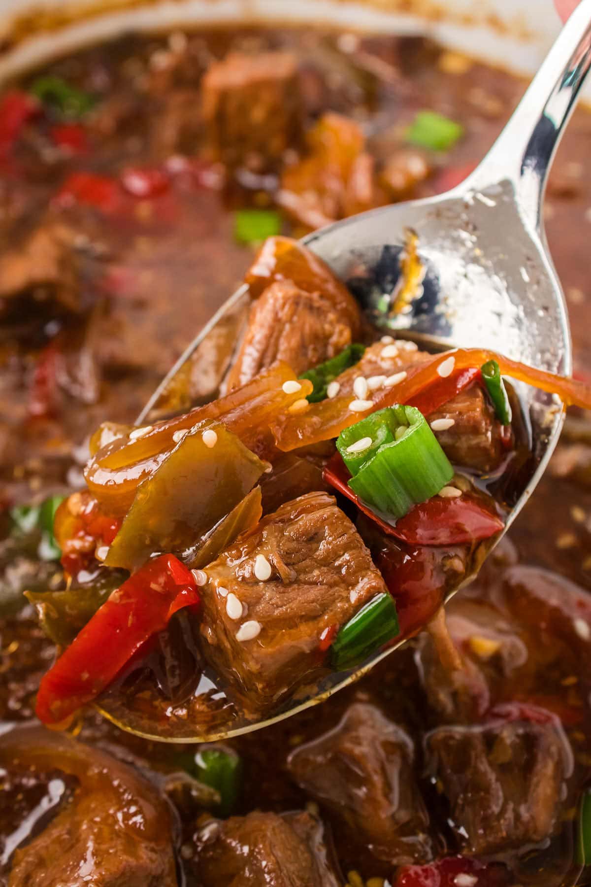 Slow cooker Chinese beef stew with peppers and onions on a spoon.