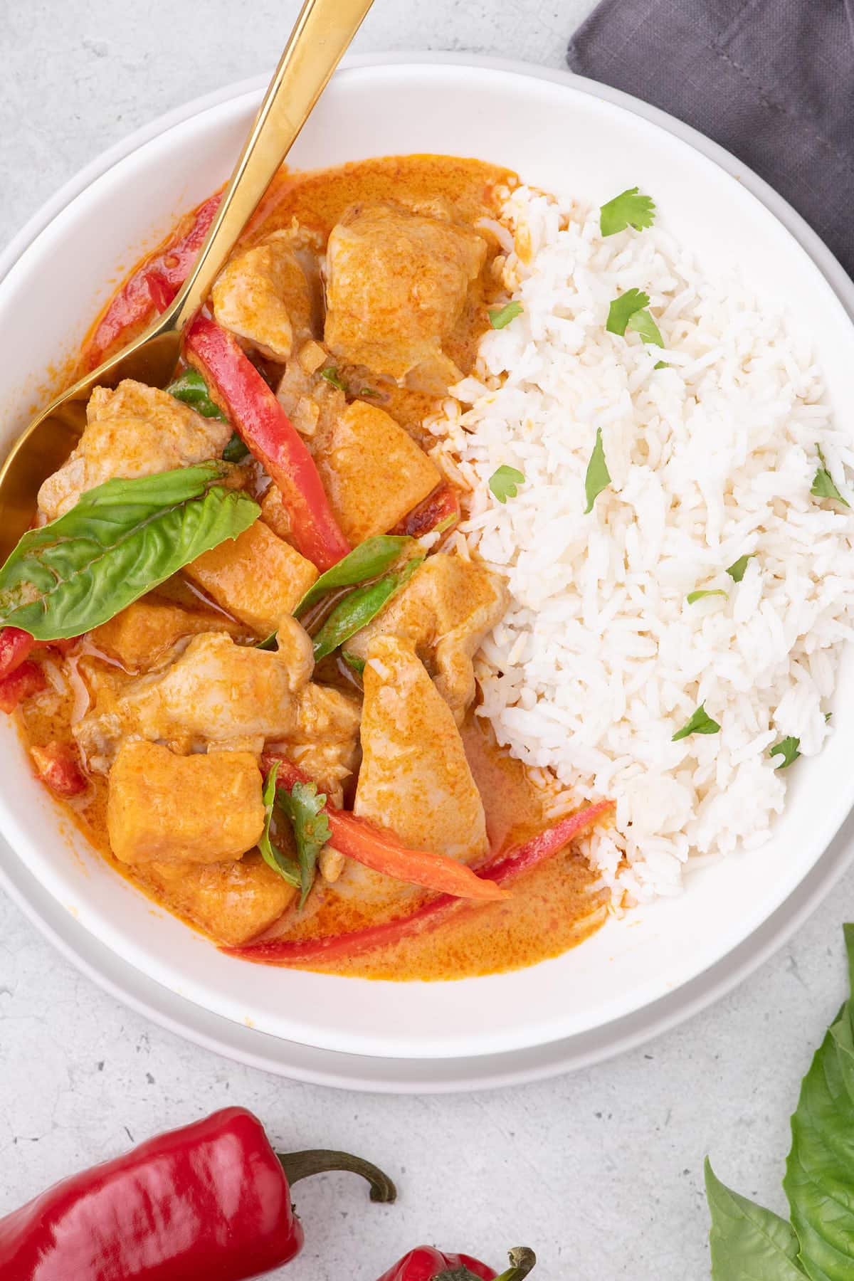 Thai Red Curry Chicken served in a white bowl alongside rice and peppers.