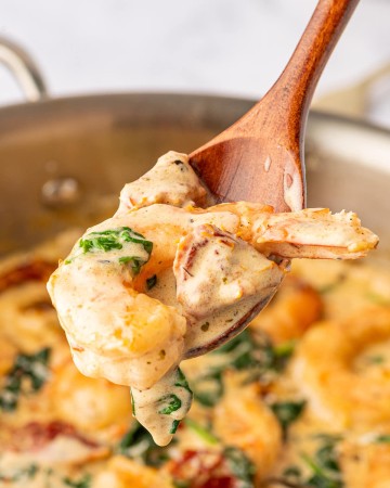 A wooden spoon is being used to scoop shrimp and spinach out of a pan.