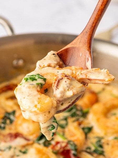 A wooden spoon is being used to scoop shrimp and spinach out of a pan.