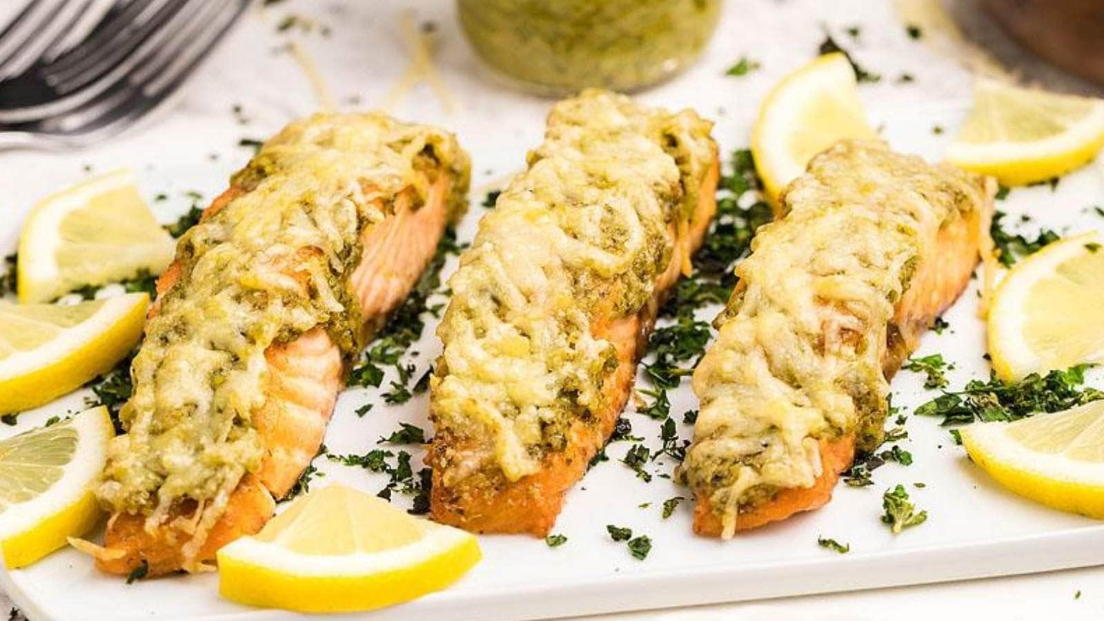 Three salmon fillets on a white plate with lemon wedges.