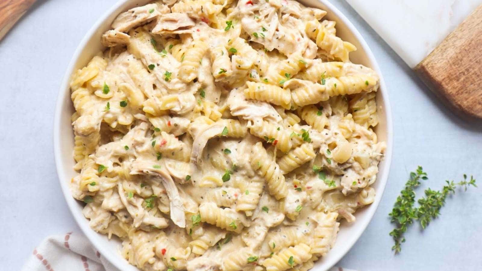Chicken pasta in a white bowl with herbs.