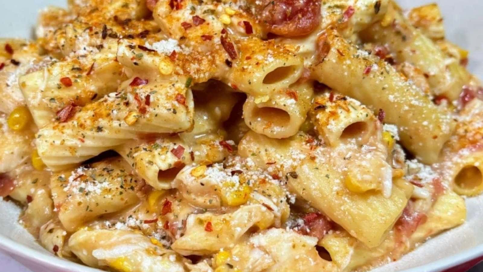 A bowl of pasta with bacon and corn.