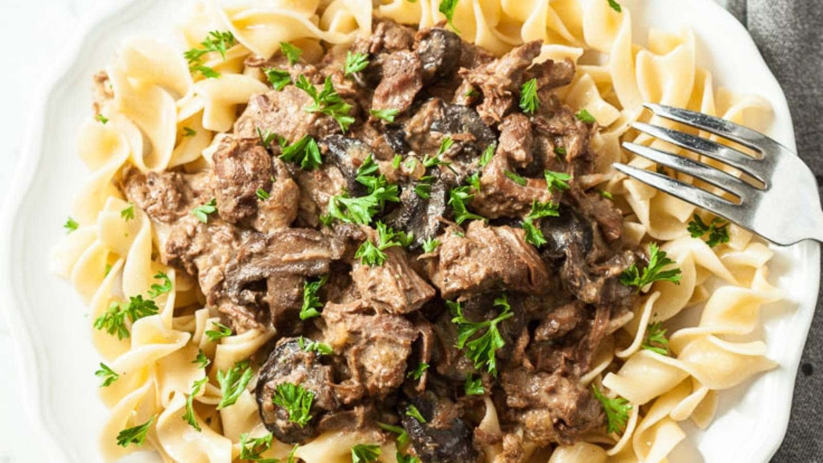 A plate of noodles with meat and mushrooms.