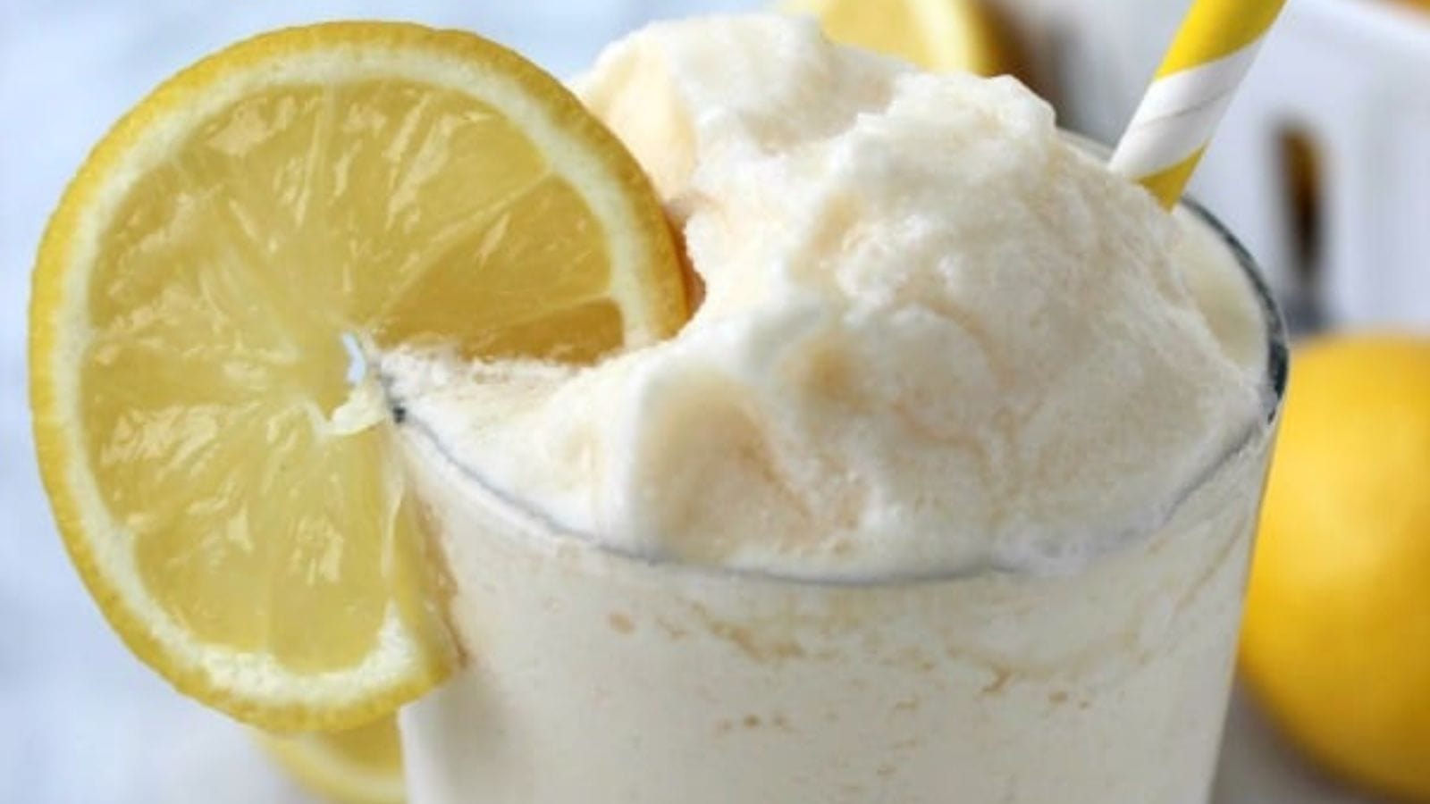 A glass of lemonade with whipped cream and lemon slices.