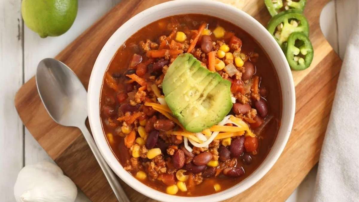 A bowl of chili with avocado and lime on a cutting board.