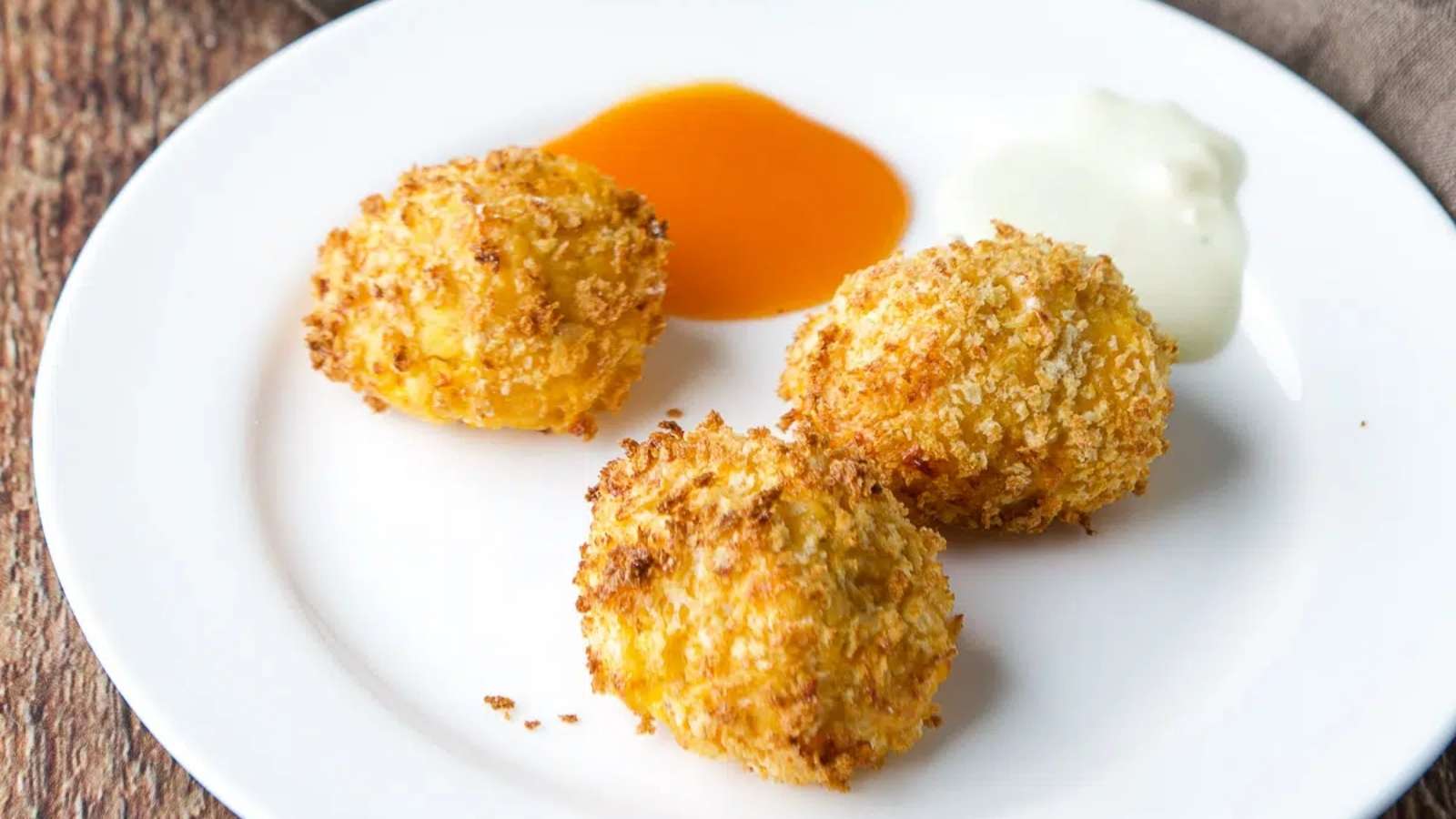Three fried potato balls on a plate with sauce.