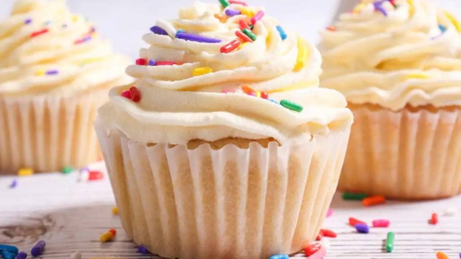 White cupcakes with sprinkles on a wooden table.