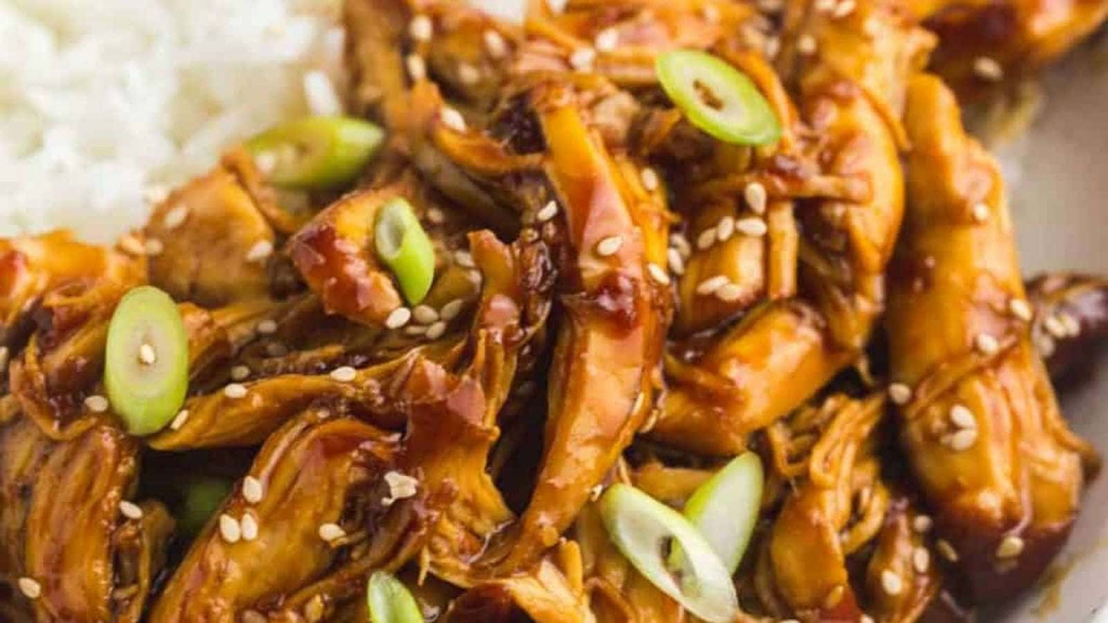 A bowl of asian chicken with rice and sesame seeds.