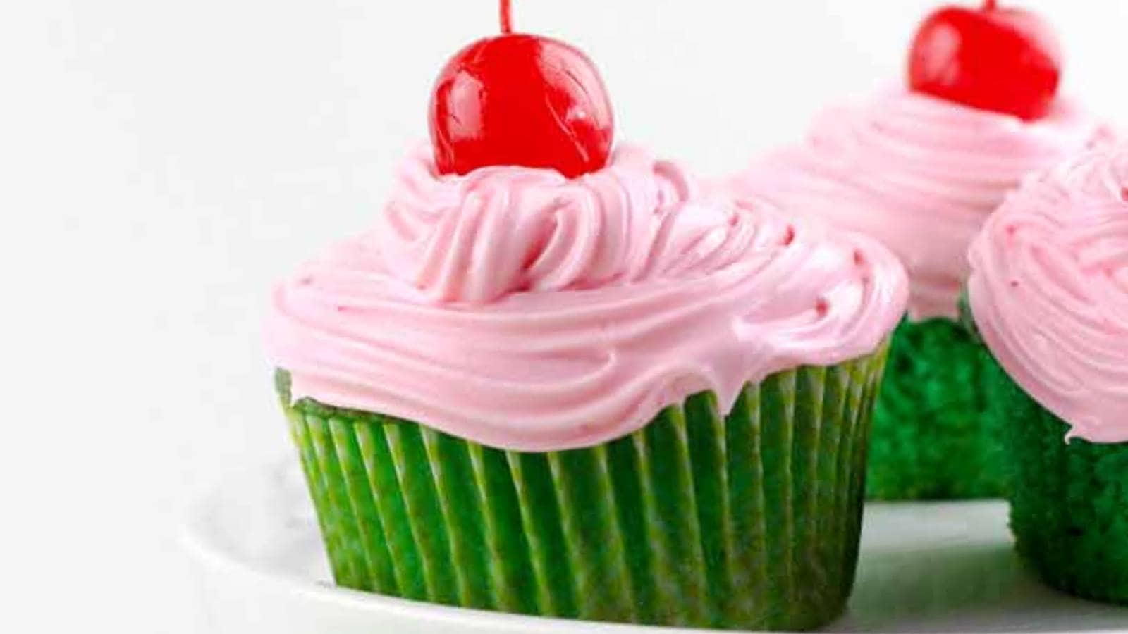 A cupcake with pink frosting and a cherry on top.
