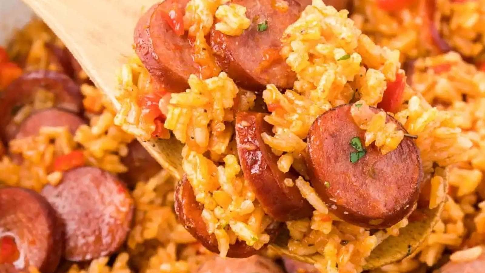 A wooden spoon full of rice and sausage.