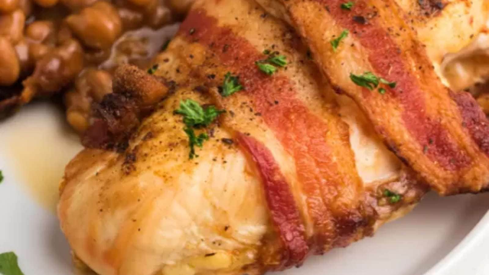 Chicken breast with bacon and beans on a white plate.