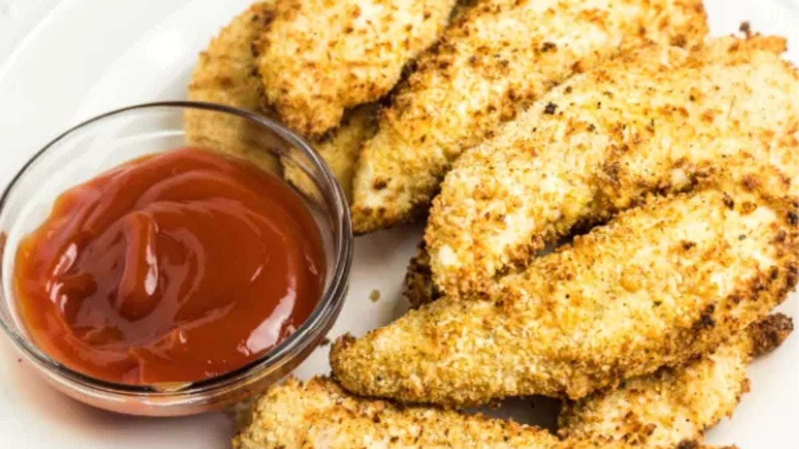Fried chicken fingers with ketchup on a plate.