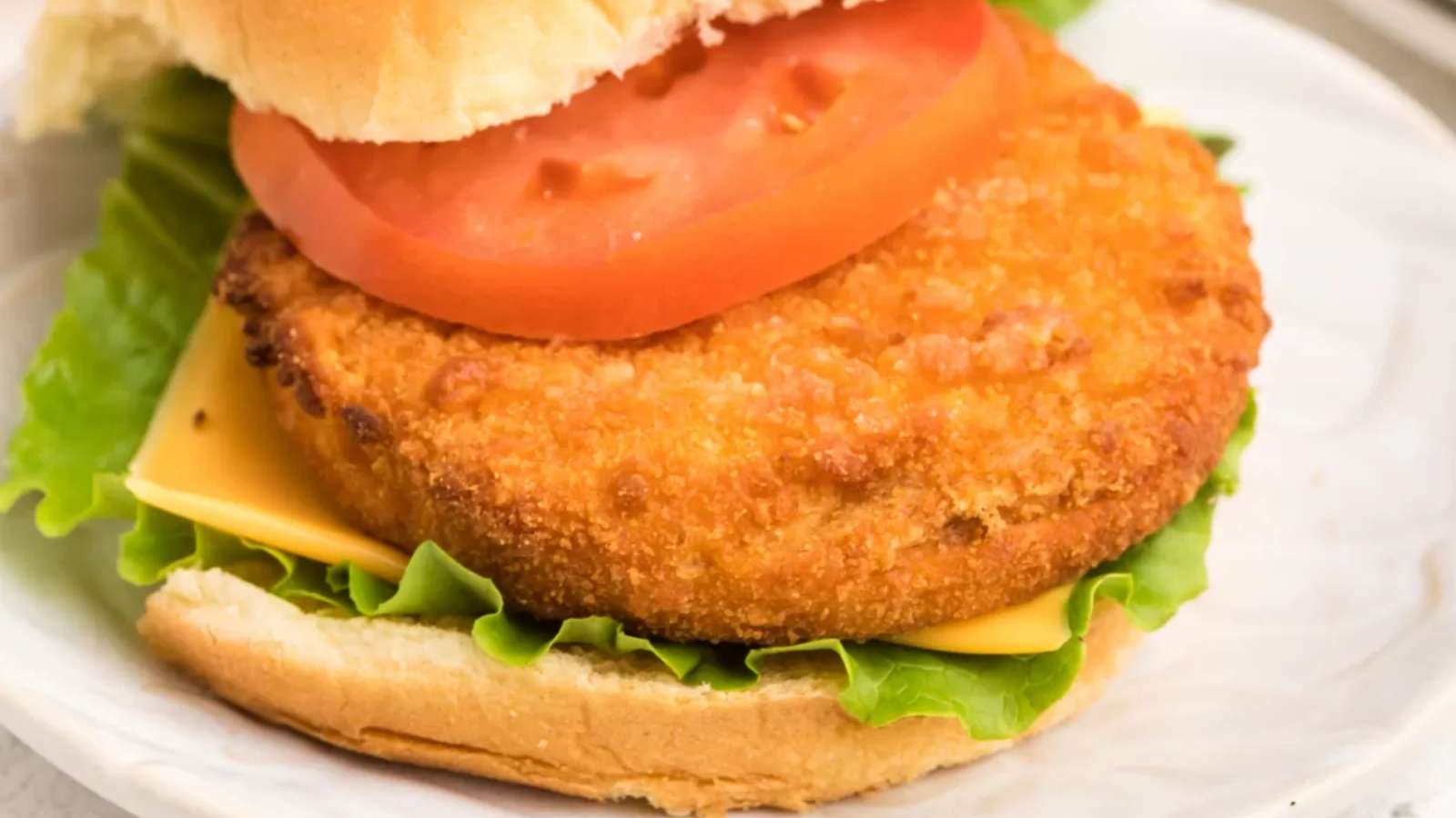 A chicken burger with tomato and lettuce on a white plate.