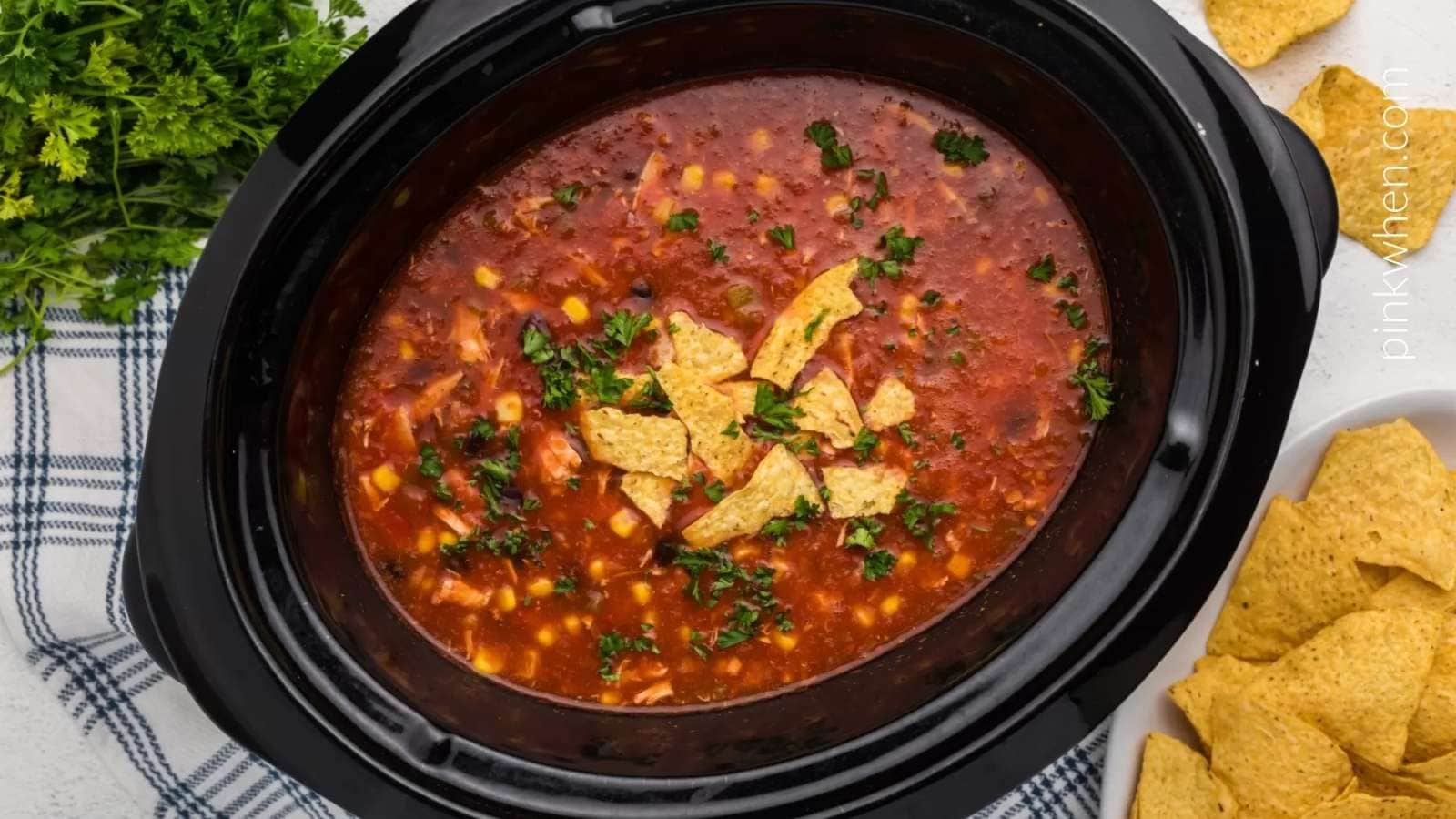 A crock pot full of mexican chili and tortilla chips.