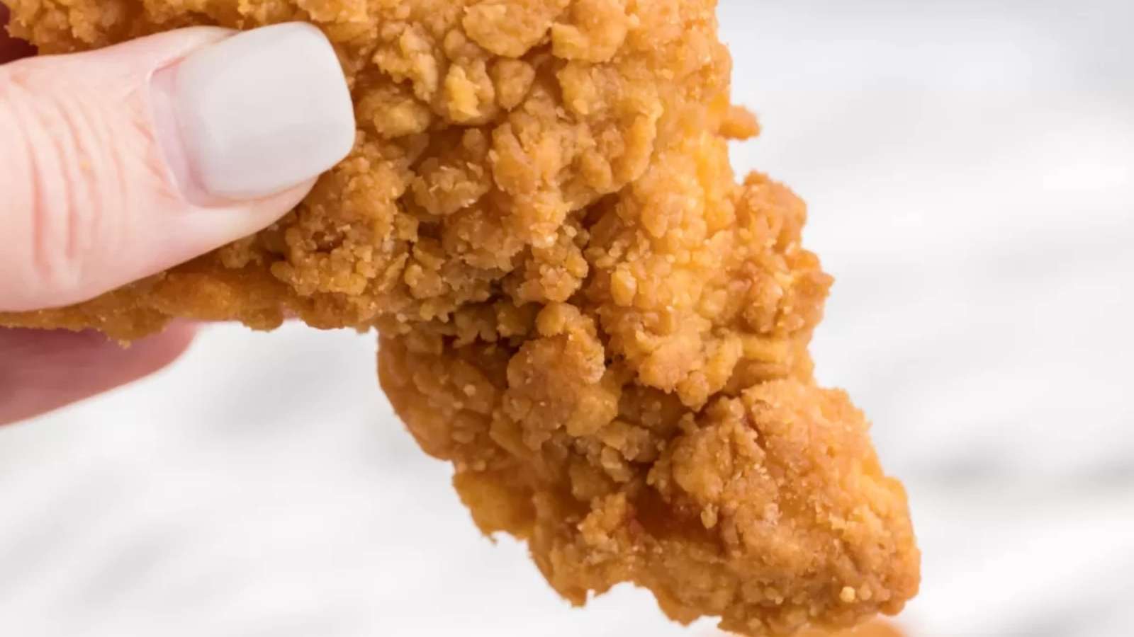 A hand holding a fried chicken.