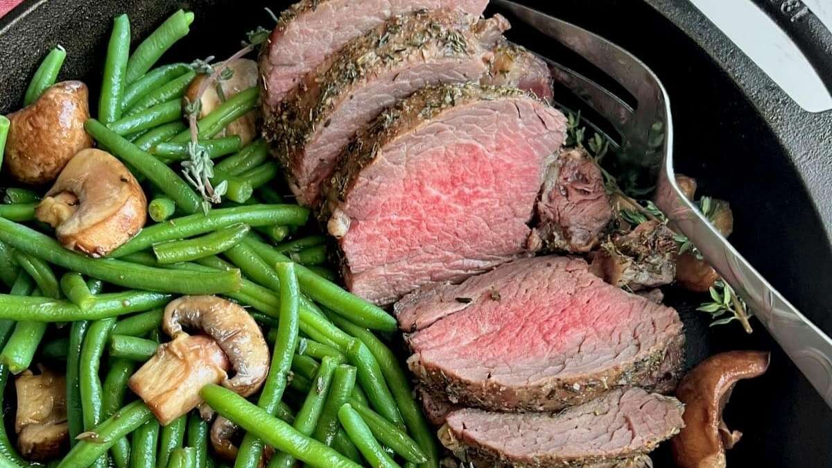 Steak with green beans and mushrooms in a skillet.