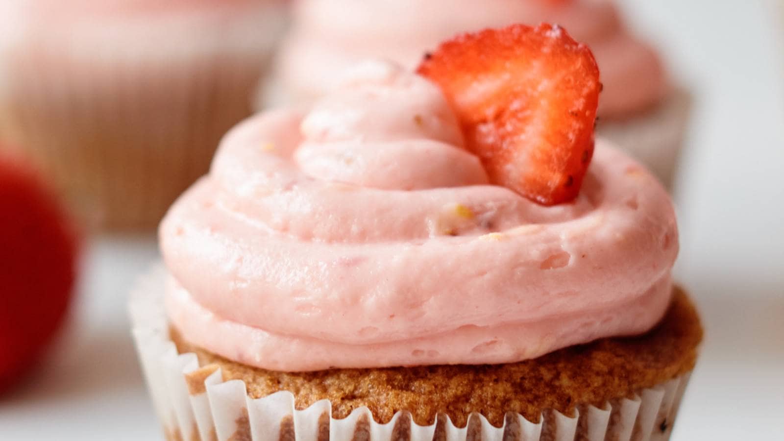 A cupcake with pink frosting and a slice of strawberry.