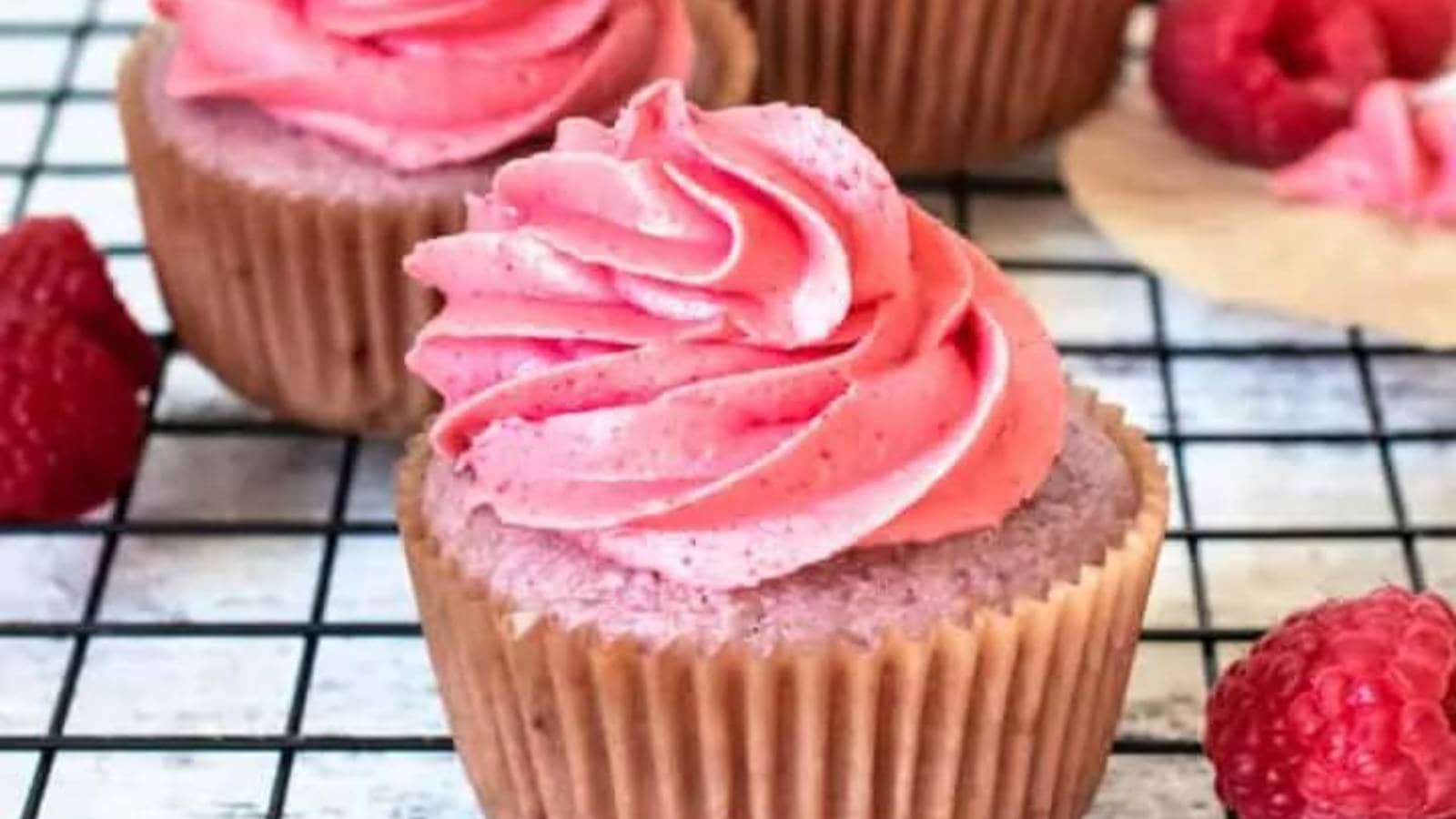 Three cupcakes with raspberry frosting on a cooling rack.