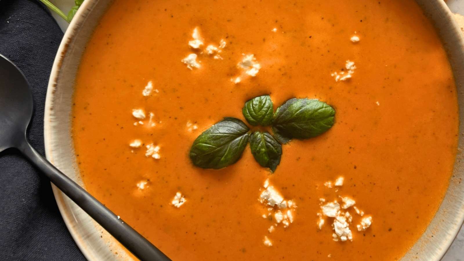 A bowl of tomato soup with basil leaves.