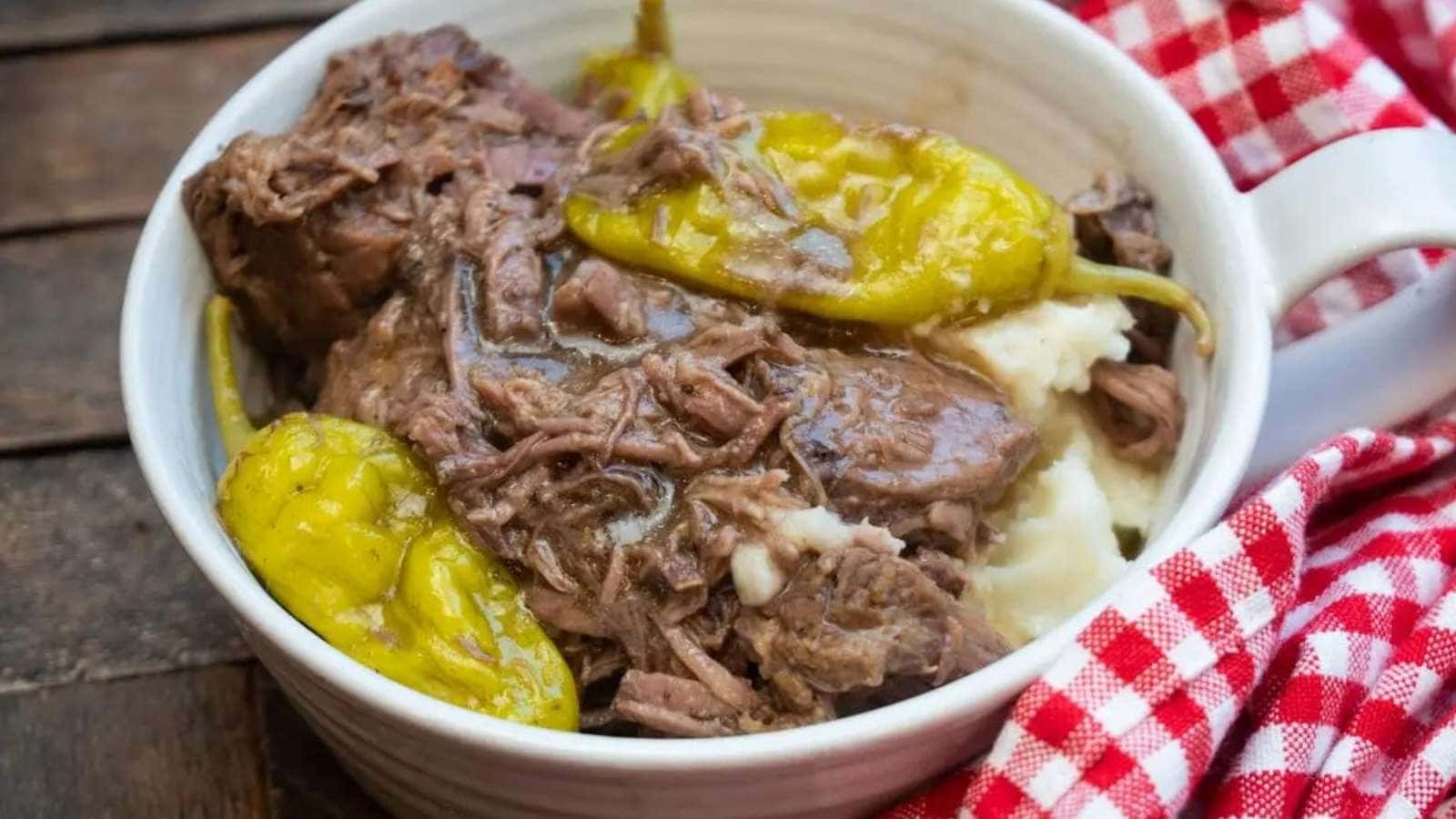 A mug of beef stew with peppers and mashed potatoes.