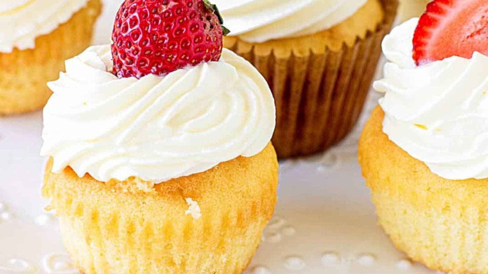 A plate of cupcakes topped with strawberries and whipped cream.