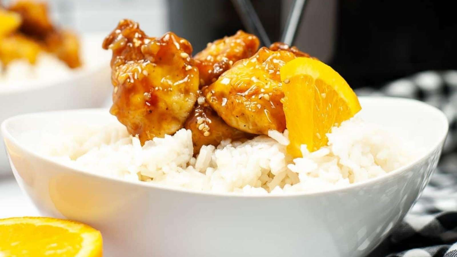 A bowl of orange chicken with rice and orange slices.