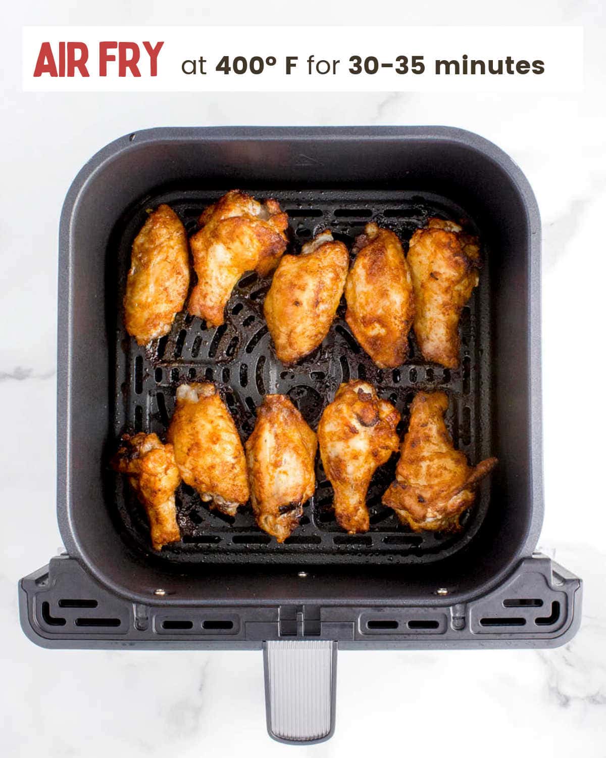 An air fryer with frozen chicken wings on it.