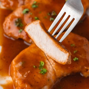 A fork is holding a piece of baked pork chops in smothered in BBQ sauce.