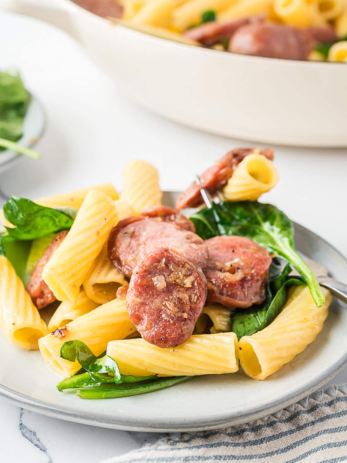 A plate of pasta with sausage and spinach.