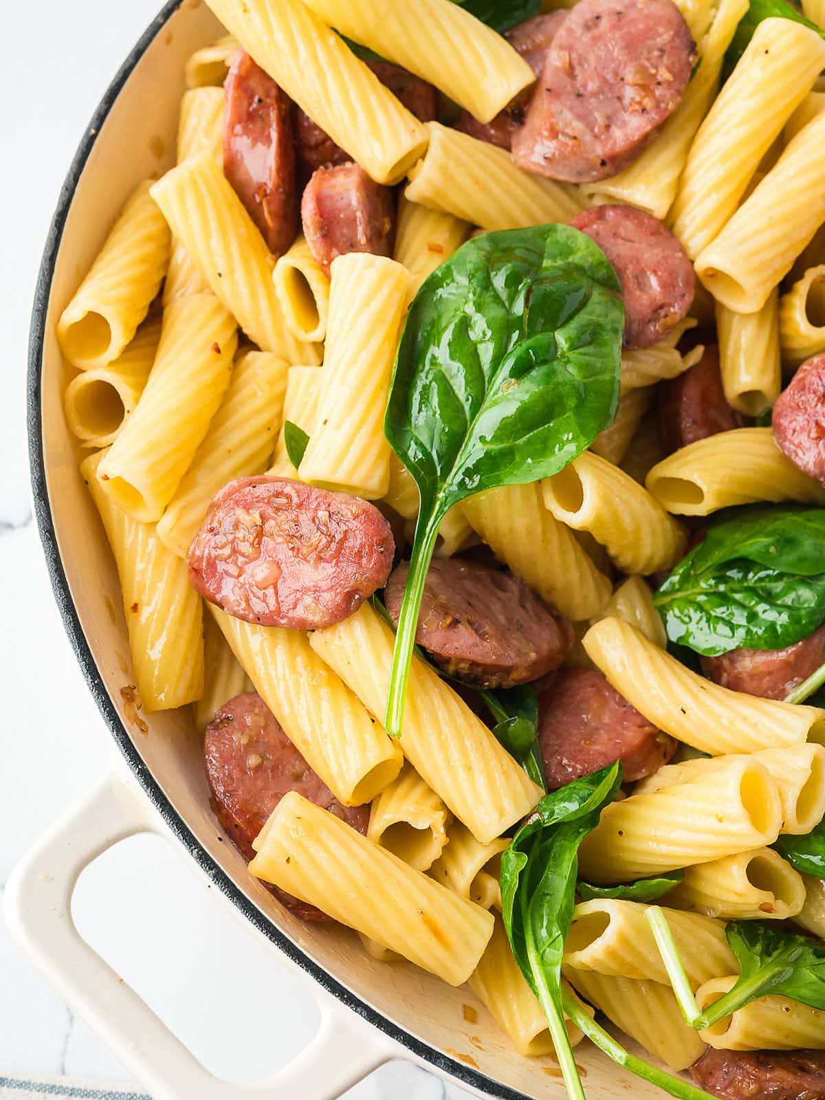 Penne with sausage and spinach in a skillet.