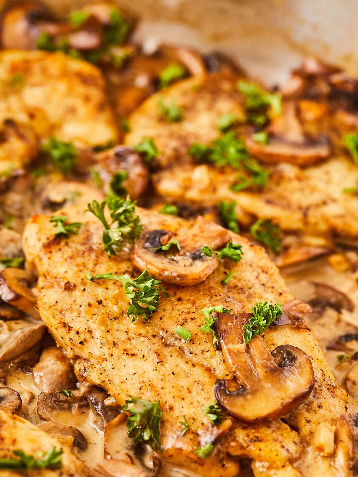 Chicken breasts with mushrooms and parsley in a skillet.