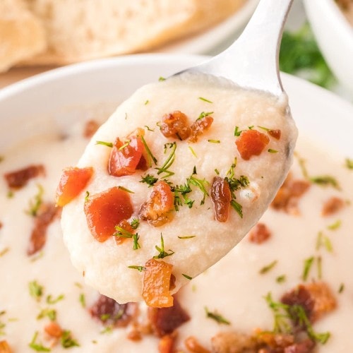 A spoon is holding a bowl of Chicken and Potato Soup.