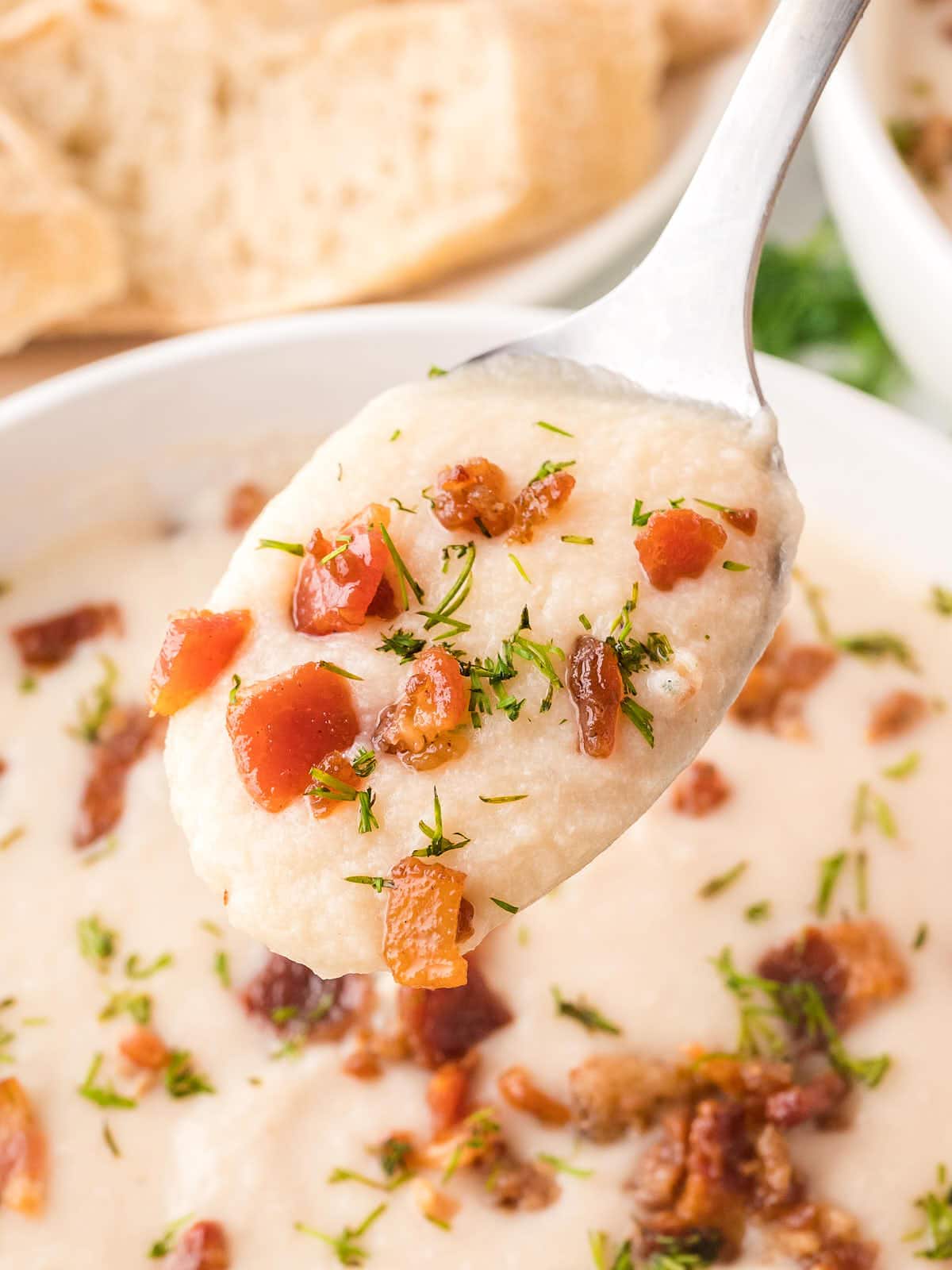 A spoon is holding a bowl of Chicken and Potato Soup.