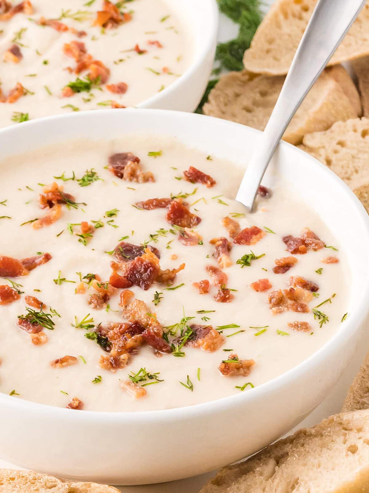 Two bowls of chicken and potato soup with bacon and bread.