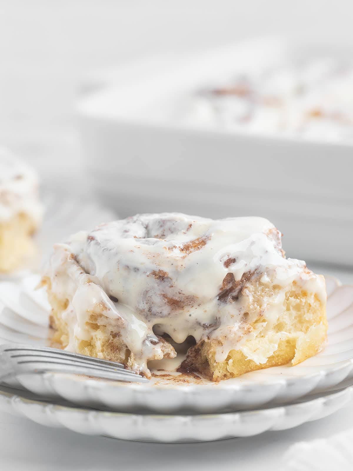 Freshly baked Cinnamon Rolls on a plate drizzled with icing, ready to be enjoyed with a fork.