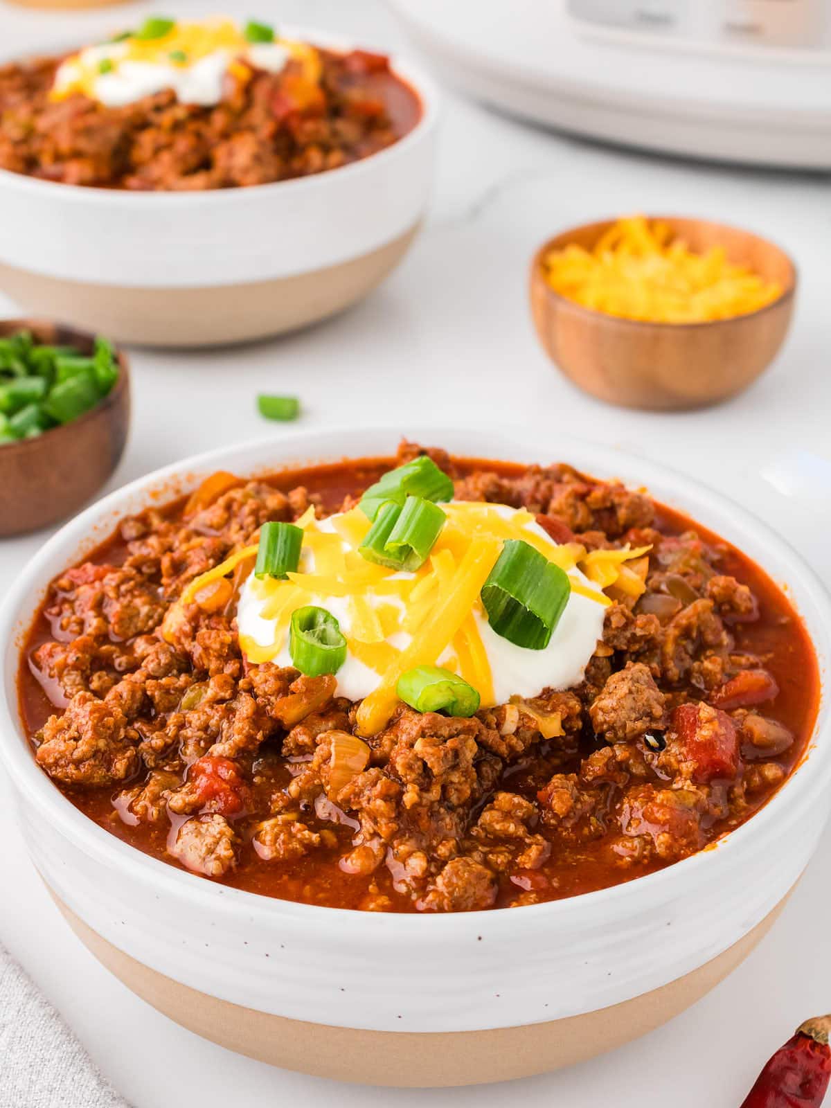 Two bowls of chili with cheese and sour cream.