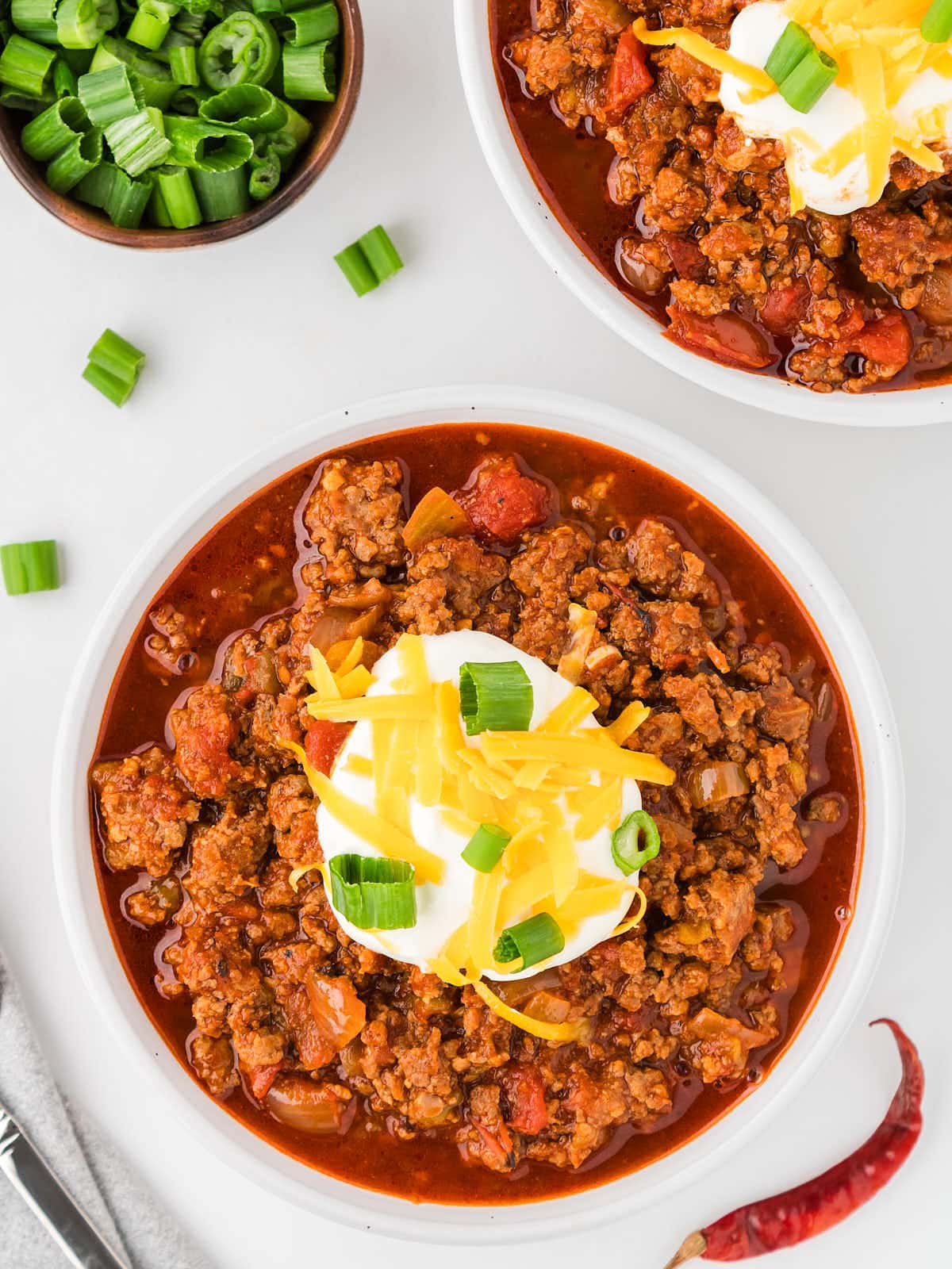 Two bowls of chili with sour cream and green onions.