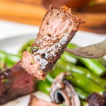 New York Strip Steak on a fork with green beans on a plate.