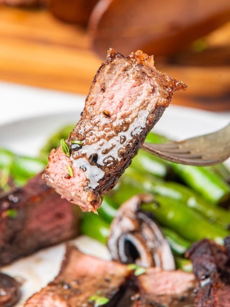 New York Strip Steak on a fork with green beans on a plate.